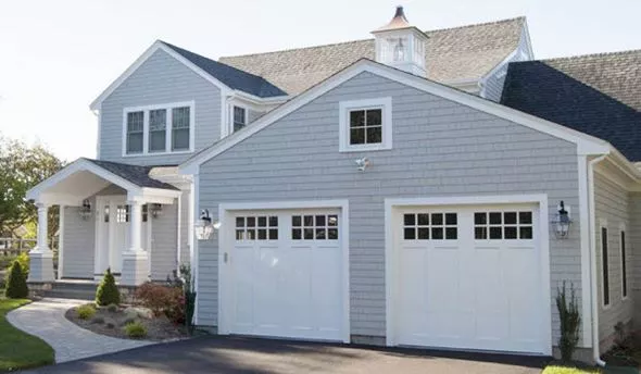 Two white Signature Carriage wood garage doors on a large home with white cedar siding.