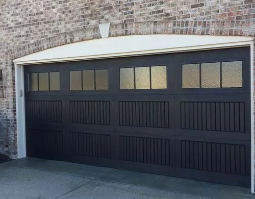 Black paneled two-car garage door with windows in the top, in a brick home.