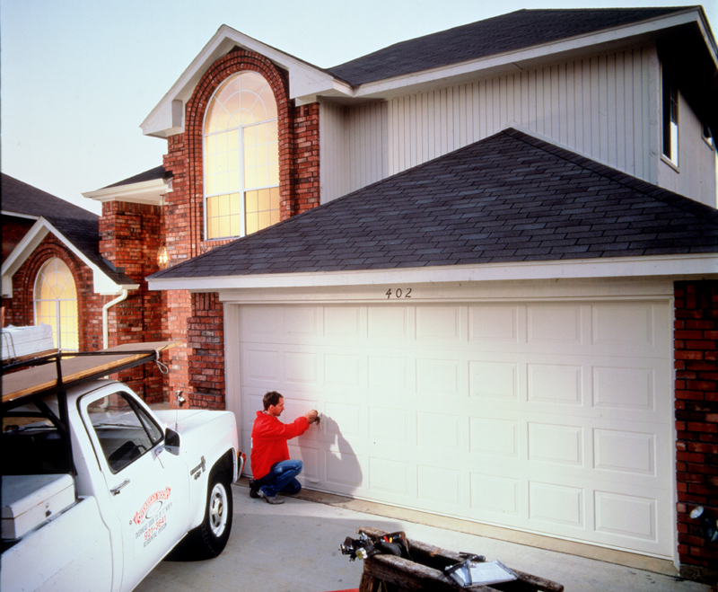 Overhead Door garage door technician fixing the exterior of a home's large white garage door